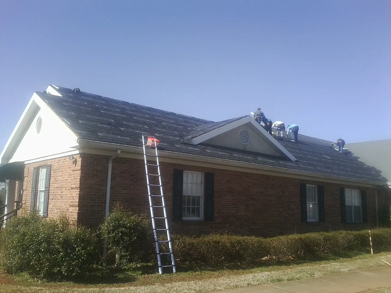Crew tearing shingles off a brick ranch roof with a ladder set — Emergency Roof Repair work by our crew in Alhambra