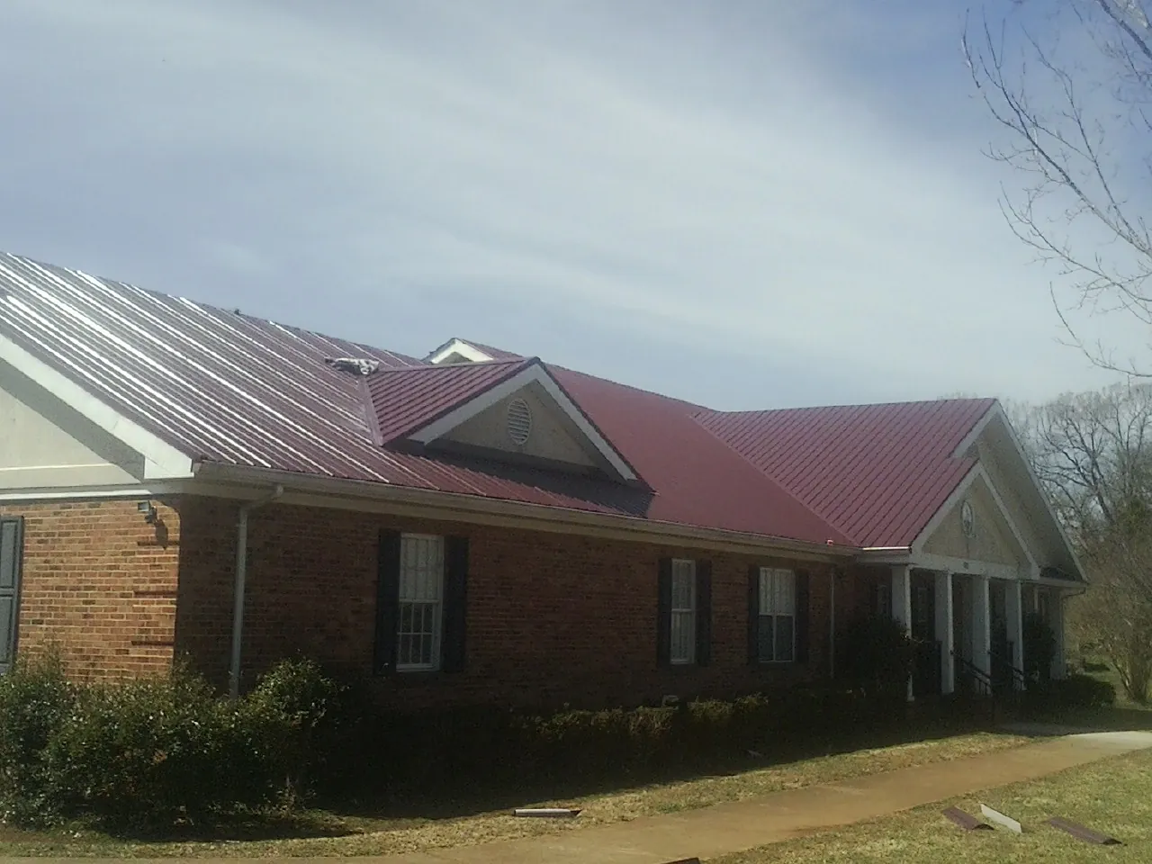 Red metal roof with gabled entries on a long brick building, from a Hail Damage Roof Repair job in Alhambra